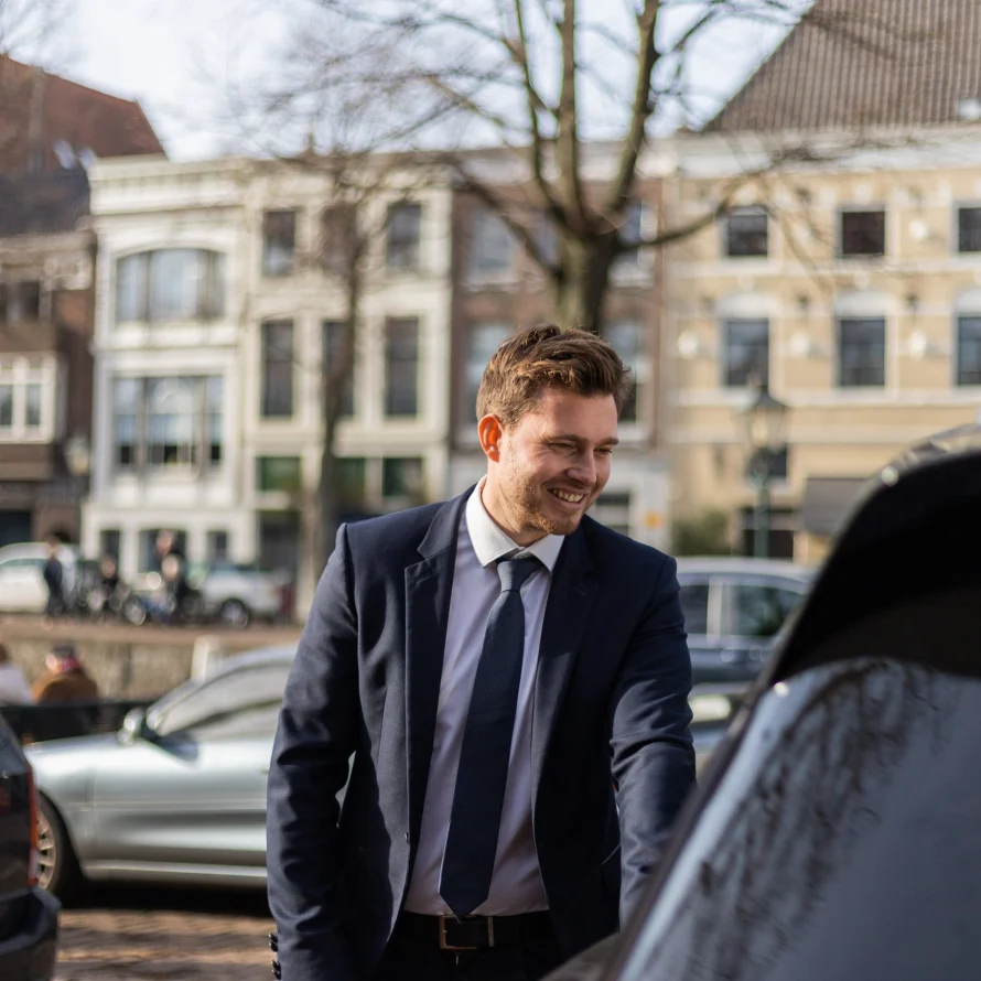 Glimlachende chauffeur van Taxi Stam in pak naast een auto in de stad