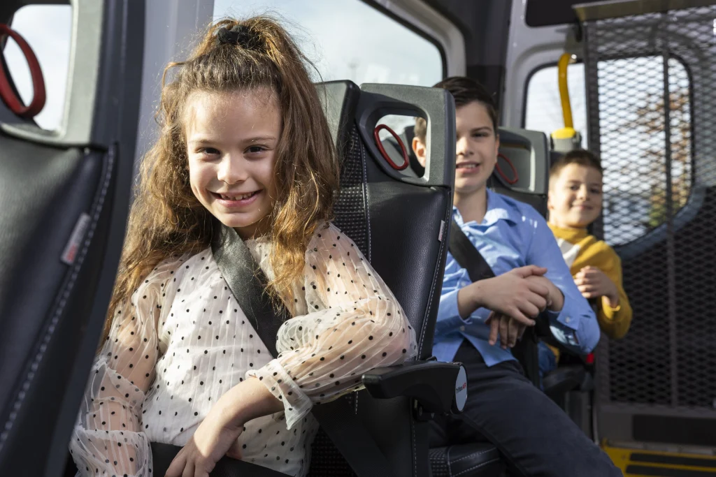 Lachend meisje met gordel om in de bus van het leerlingenvervoer