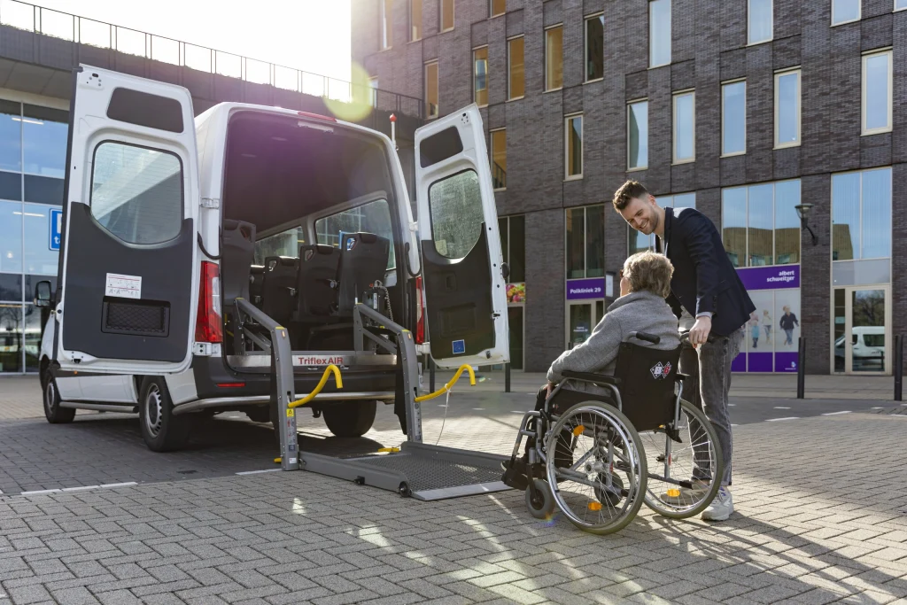 Chauffeur helpt een passagier in een rolstoel via de lift de bus in