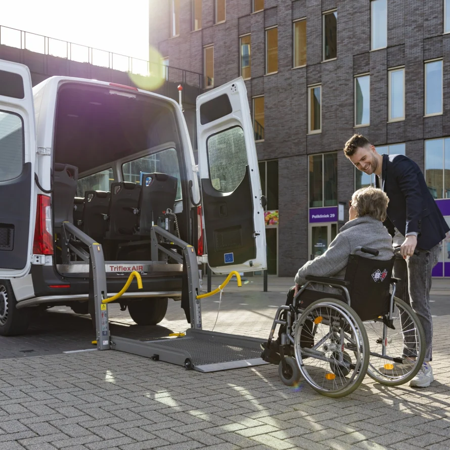 Chauffeur helpt een passagier in een rolstoel via de lift de bus in