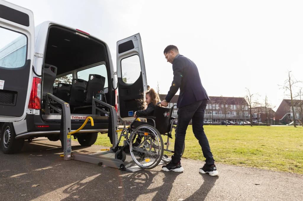 Chauffeur begeleidt een passagier in een rolstoel bij de bus
