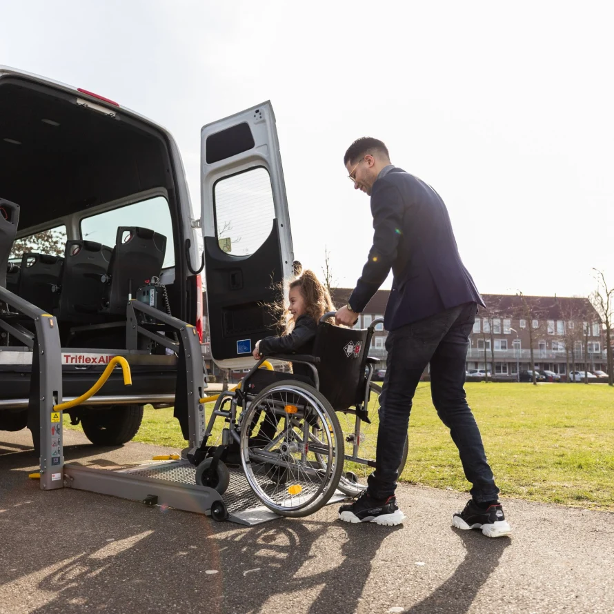 Chauffeur begeleidt een passagier in een rolstoel bij de bus