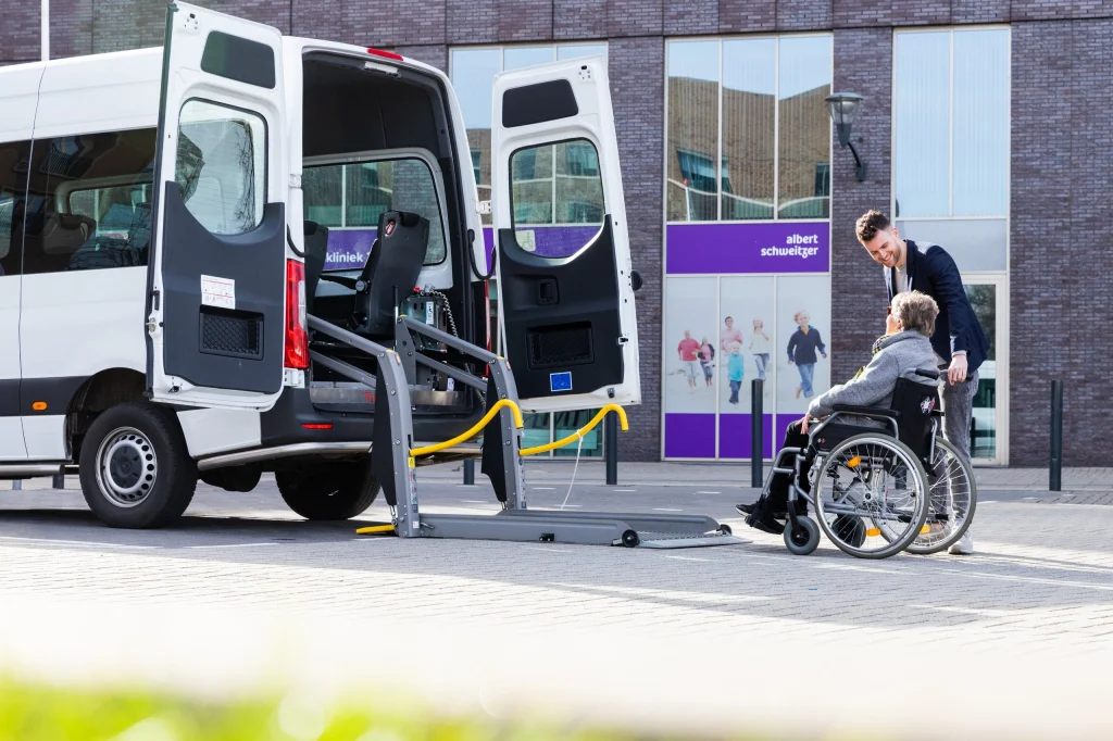 Chauffeur helpt een passagier in een rolstoel bij de rolstoelbus
