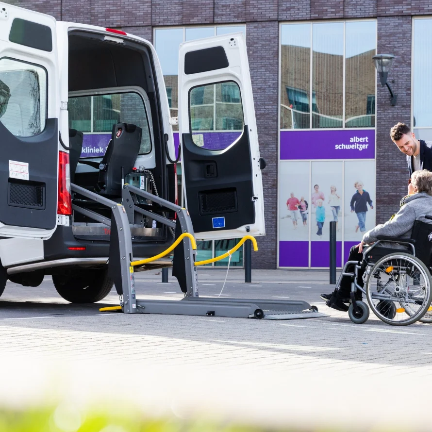 Chauffeur helpt een passagier in een rolstoel bij de rolstoelbus