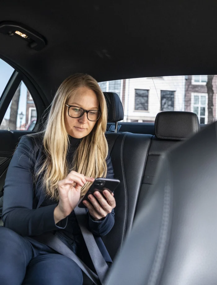 Zakenvrouw met telefoon op de achterbank van een zakelijke taxi
